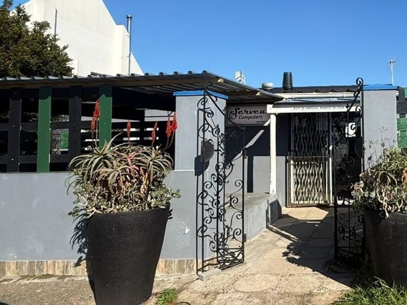Front entrance of a commercial property featuring a paved walkway, security gate, and corrugated metal roofing.