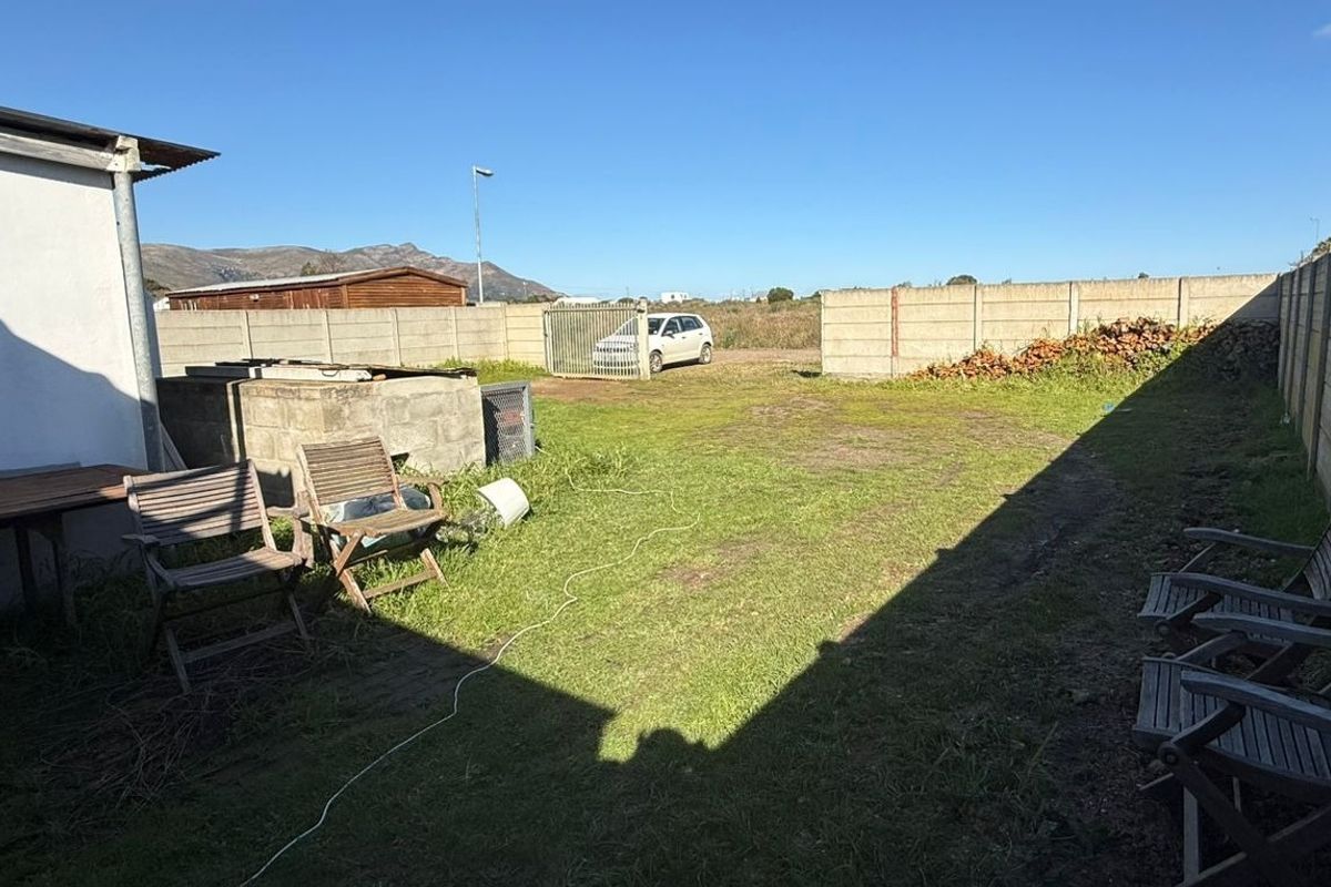 A spacious rear yard featuring a precast concrete boundary wall, metal gate access, and a small concrete block structure.
