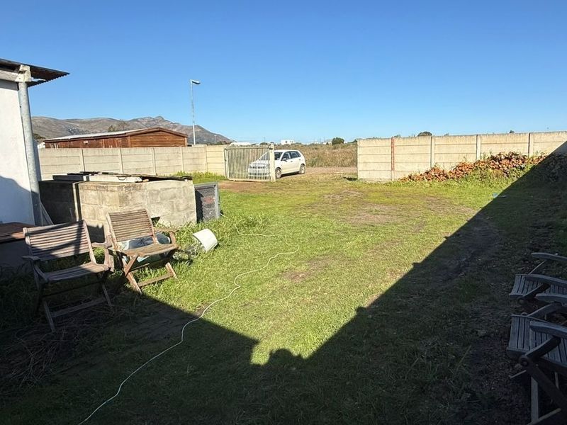 A spacious rear yard featuring a precast concrete boundary wall, metal gate access, and a small concrete block structure.