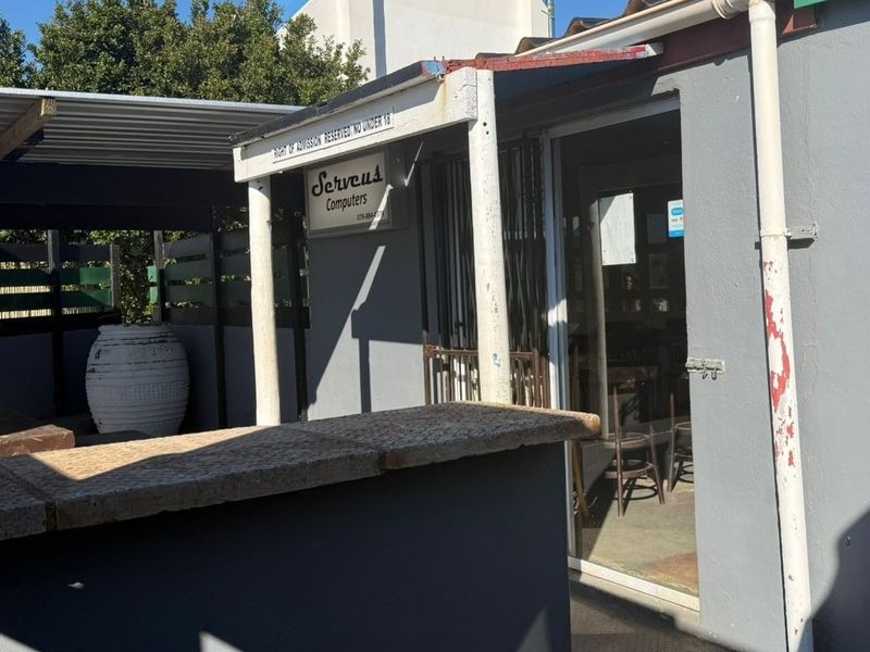 A covered outdoor patio area featuring a stone-topped counter, sliding glass door entrance, and timber privacy screening, suitable for business or commercial use.