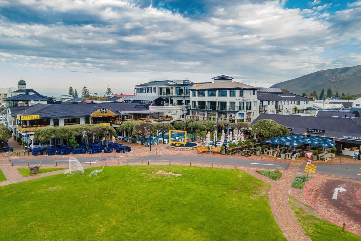 Aerial view of a commercial waterfront complex featuring paved courtyards, landscaped gardens, and multi-story buildings with various retail and dining establishments.