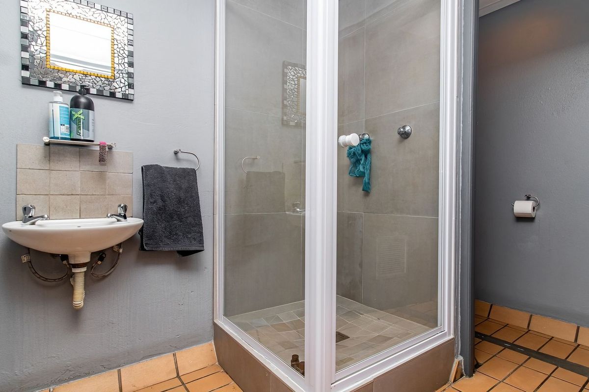 A functional bathroom featuring a corner shower enclosure, wall-mounted basin with tiled splashback, and tiled flooring.