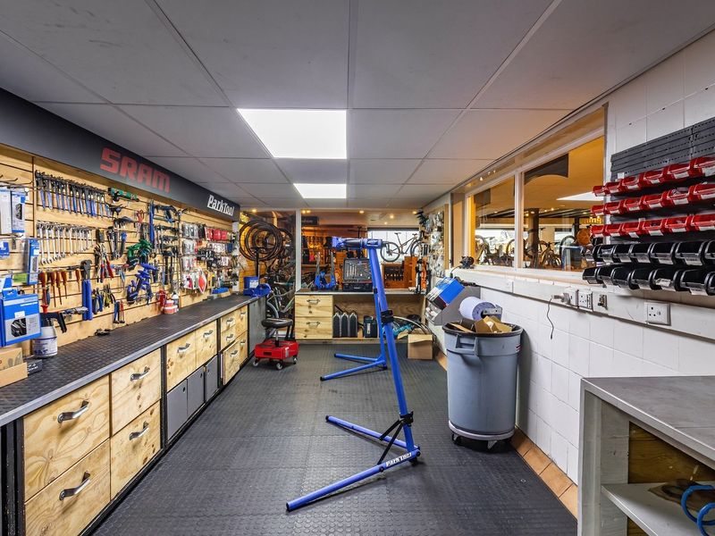 A well-organized professional bicycle workshop featuring extensive wall-mounted tool storage, durable rubber flooring, and integrated workbench cabinetry.