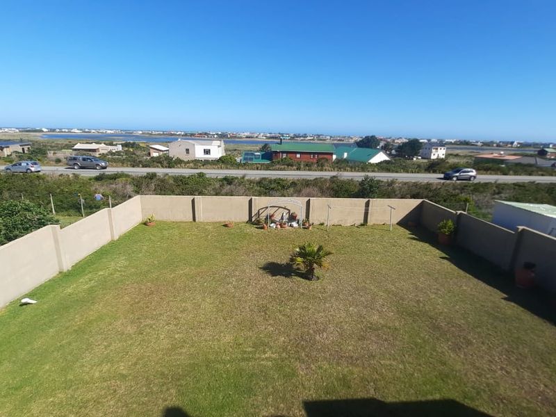 A spacious, enclosed backyard featuring a well-maintained lawn and perimeter wall, offering expansive views of the surrounding landscape and coastal area.