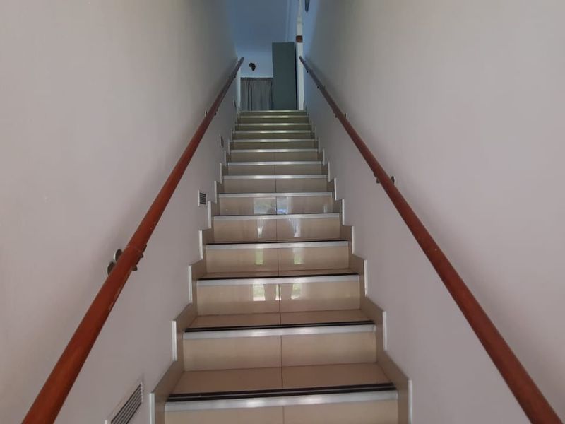 A clean, well-maintained staircase featuring tiled steps with safety nosing and dual wooden handrails leading to an upper level.