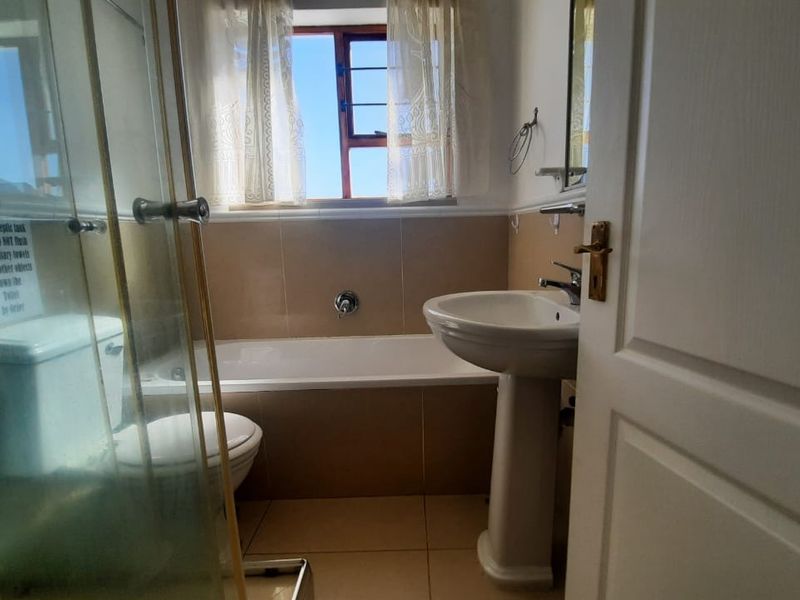 A functional bathroom featuring a pedestal basin, bathtub, and separate shower enclosure with tiled finishes and natural light.