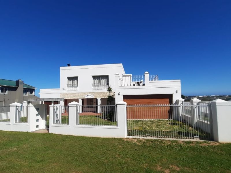 A modern two-story residential property featuring a white facade, stone accents, a balcony, and secure perimeter fencing with an integrated garage.