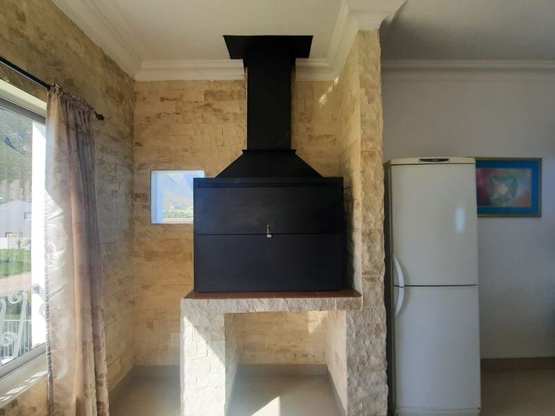 Living area featuring a prominent built-in braai with stone cladding and a black extractor hood, set against a neutral interior backdrop.