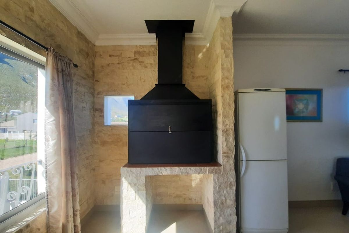 Living area featuring a prominent built-in braai with stone cladding and a black extractor hood, set against a neutral interior backdrop.