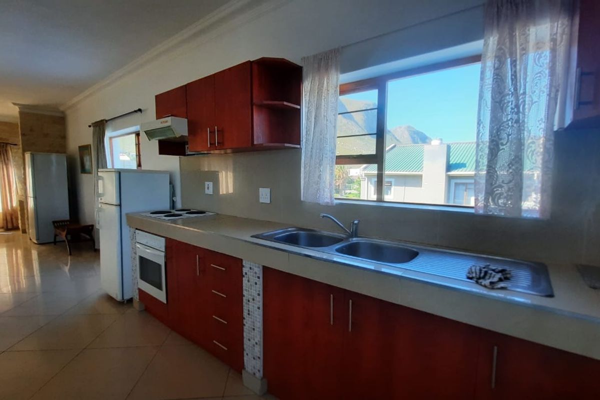 A functional kitchen featuring wooden cabinetry, a double sink, built-in oven, and electric hob, with tiled flooring and views of the surrounding area.
