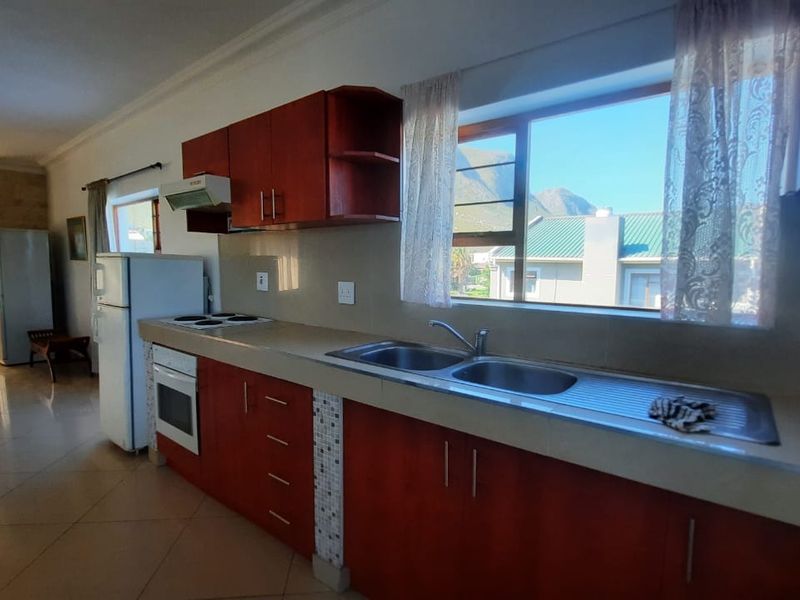A functional kitchen featuring wooden cabinetry, a double sink, built-in oven, and electric hob, with tiled flooring and views of the surrounding area.