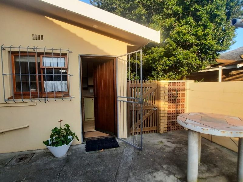 Rear exterior view of the apartment featuring a concrete patio, security gate, and access door with security bars on the window.