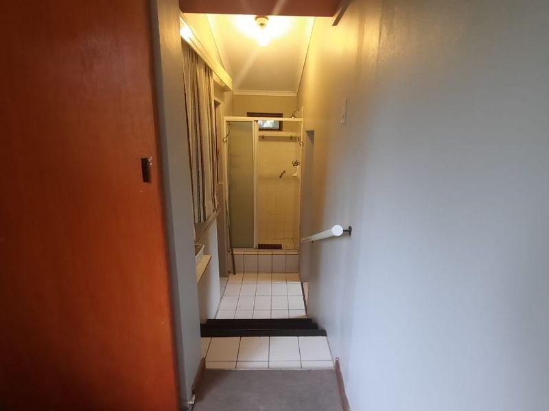 A hallway leading to a bathroom area featuring tiled flooring and a shower enclosure.