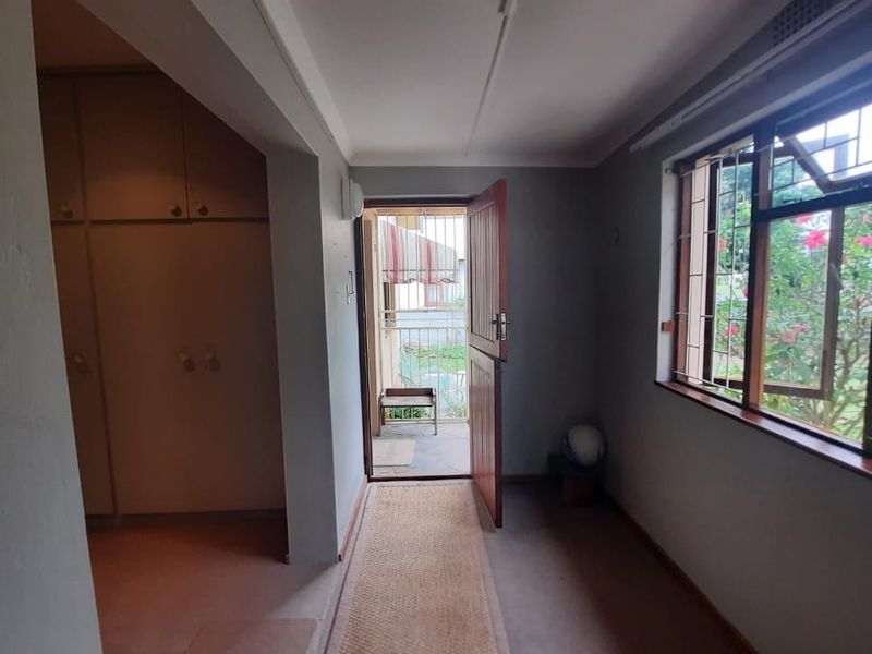 A bedroom featuring built-in cupboards, steel-framed windows, and direct access to an outdoor area through a timber door.