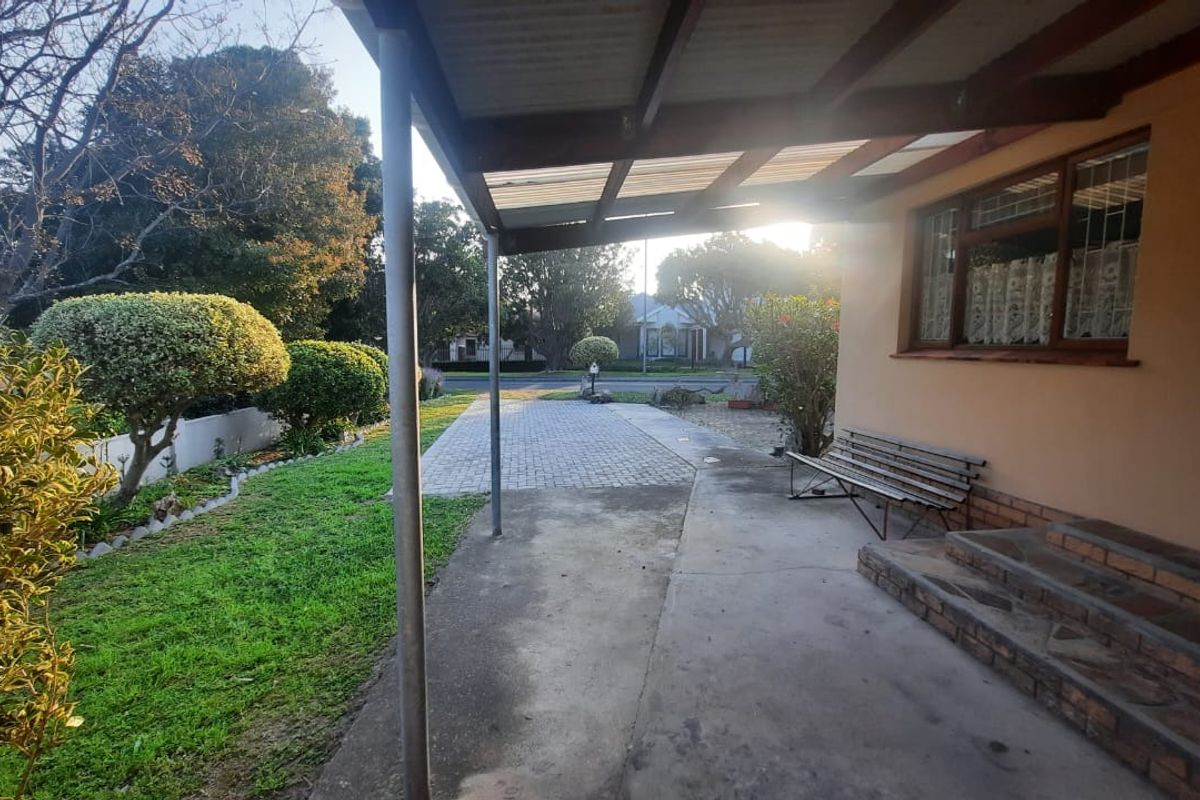A covered outdoor patio area featuring brick steps, concrete flooring, and a timber roof structure overlooking the front garden and paved driveway.