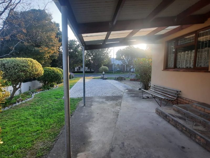 A covered outdoor patio area featuring brick steps, concrete flooring, and a timber roof structure overlooking the front garden and paved driveway.