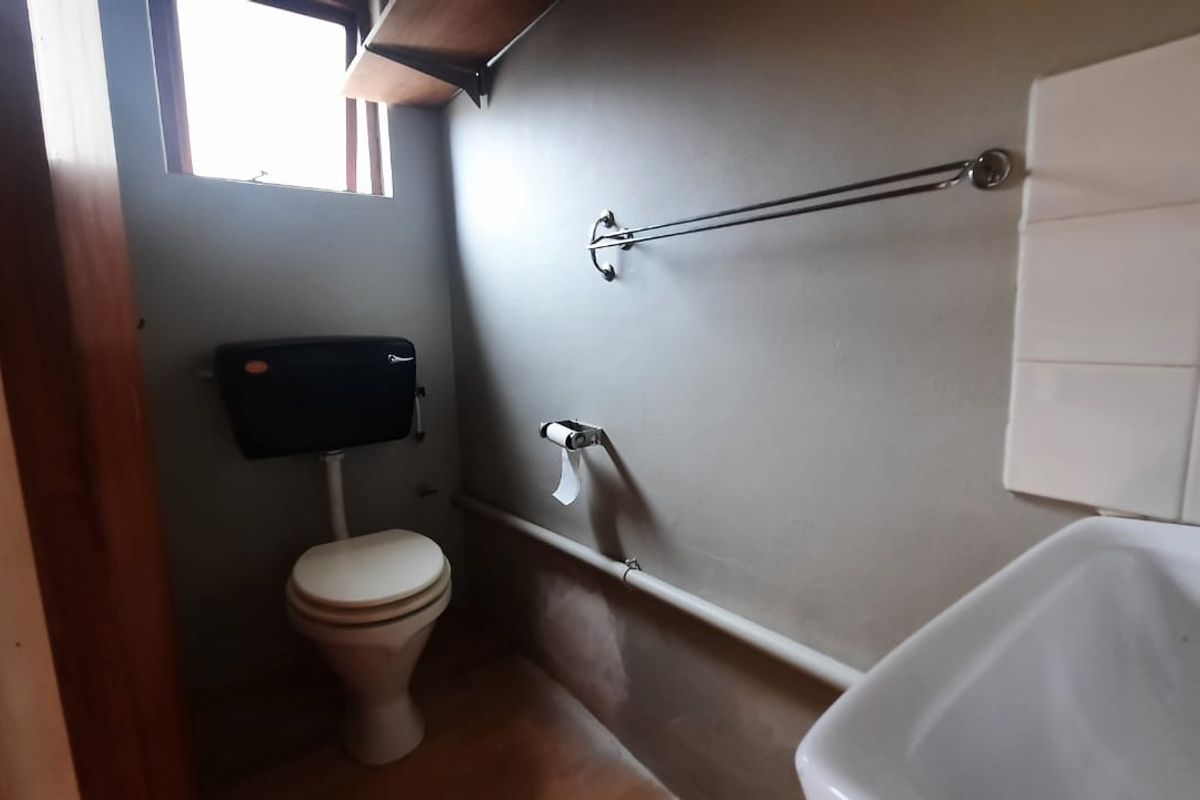 A compact bathroom featuring a standard toilet, wall-mounted washbasin, and basic fixtures, requiring cosmetic updates to improve the overall finish.