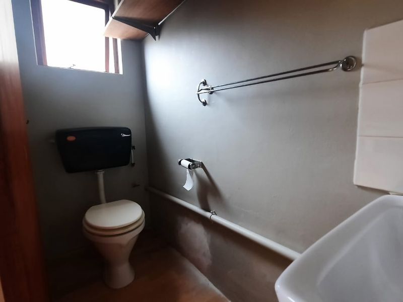 A compact bathroom featuring a standard toilet, wall-mounted washbasin, and basic fixtures, requiring cosmetic updates to improve the overall finish.