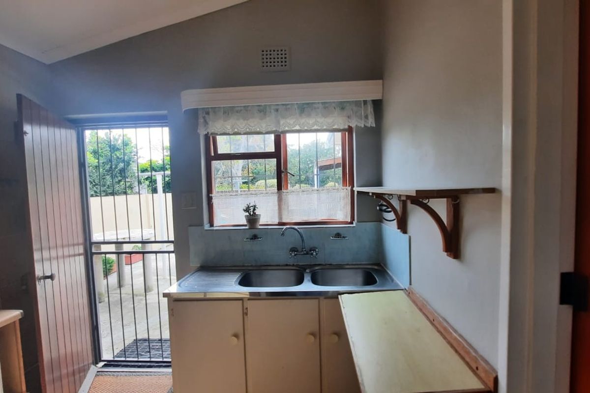 A functional kitchen area featuring a double stainless steel sink, built-in cabinetry, and direct access to an outdoor space through a security gate.