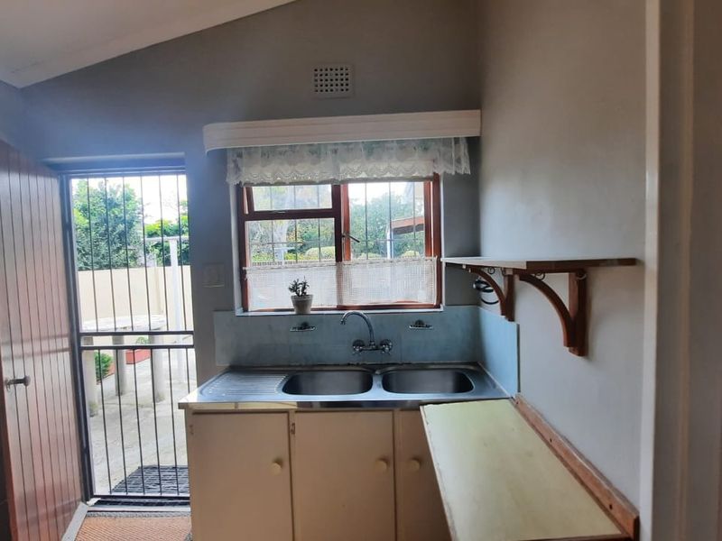 A functional kitchen area featuring a double stainless steel sink, built-in cabinetry, and direct access to an outdoor space through a security gate.