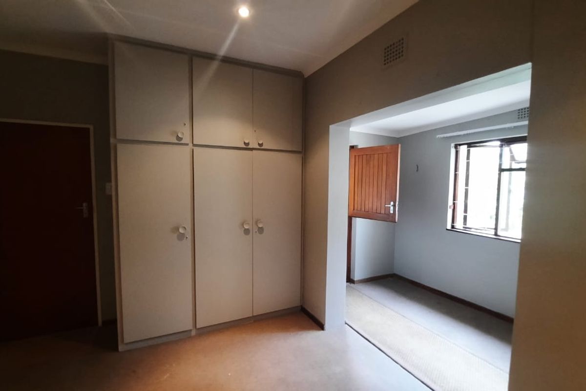An empty bedroom featuring built-in cupboards, recessed lighting, and a window with security bars, offering a neutral canvas for personalization.