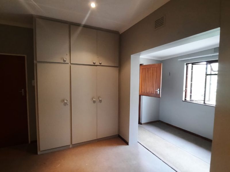 An empty bedroom featuring built-in cupboards, recessed lighting, and a window with security bars, offering a neutral canvas for personalization.