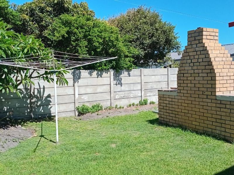 Rear garden area featuring a built-in brick braai, lawn, and perimeter precast concrete walling.
