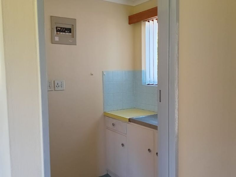 A compact scullery area featuring built-in cabinetry, a sink with a tiled splashback, and an integrated electrical distribution board.