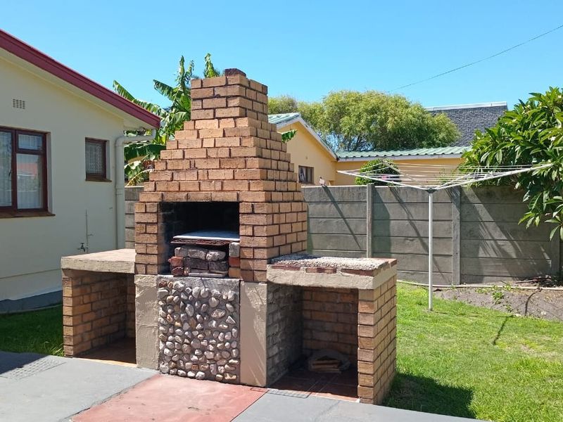 Rear garden area featuring a built-in brick braai, concrete patio space, and precast boundary walling.