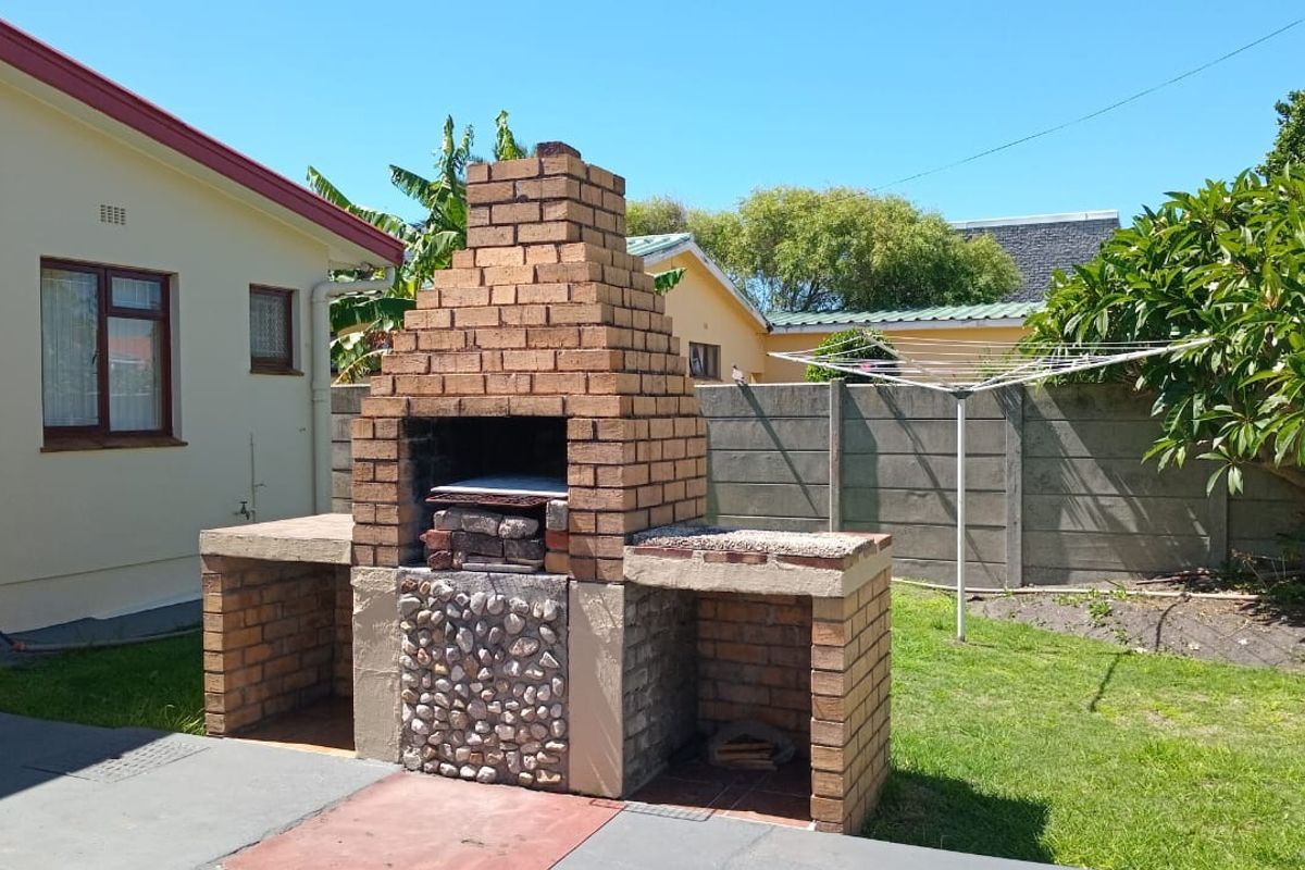 Rear garden area featuring a built-in brick braai, concrete patio space, and precast boundary walling.