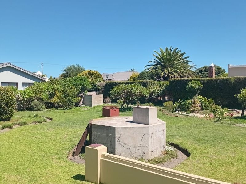 A spacious rear garden featuring a large lawn, established hedging, and a prominent central concrete structure.