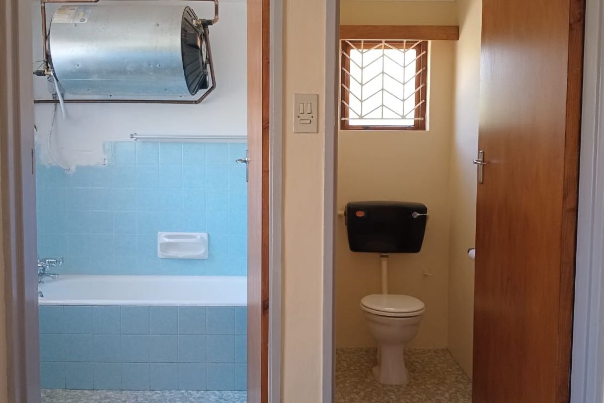 A functional bathroom and separate toilet area featuring a bathtub, tiled splashbacks, and an exposed electric water heater, requiring cosmetic updates.