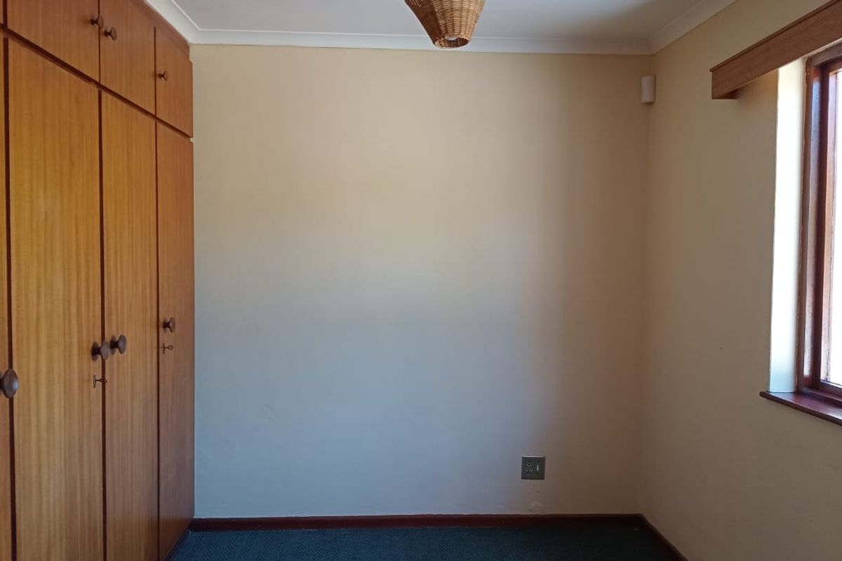 A vacant bedroom featuring built-in wooden cupboards, timber window frames, and neutral wall finishes.