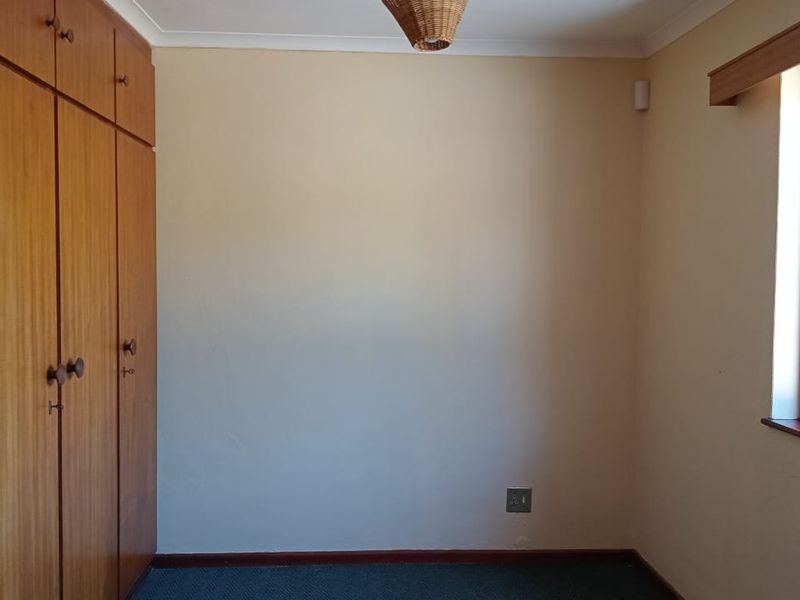 A vacant bedroom featuring built-in wooden cupboards, timber window frames, and neutral wall finishes.