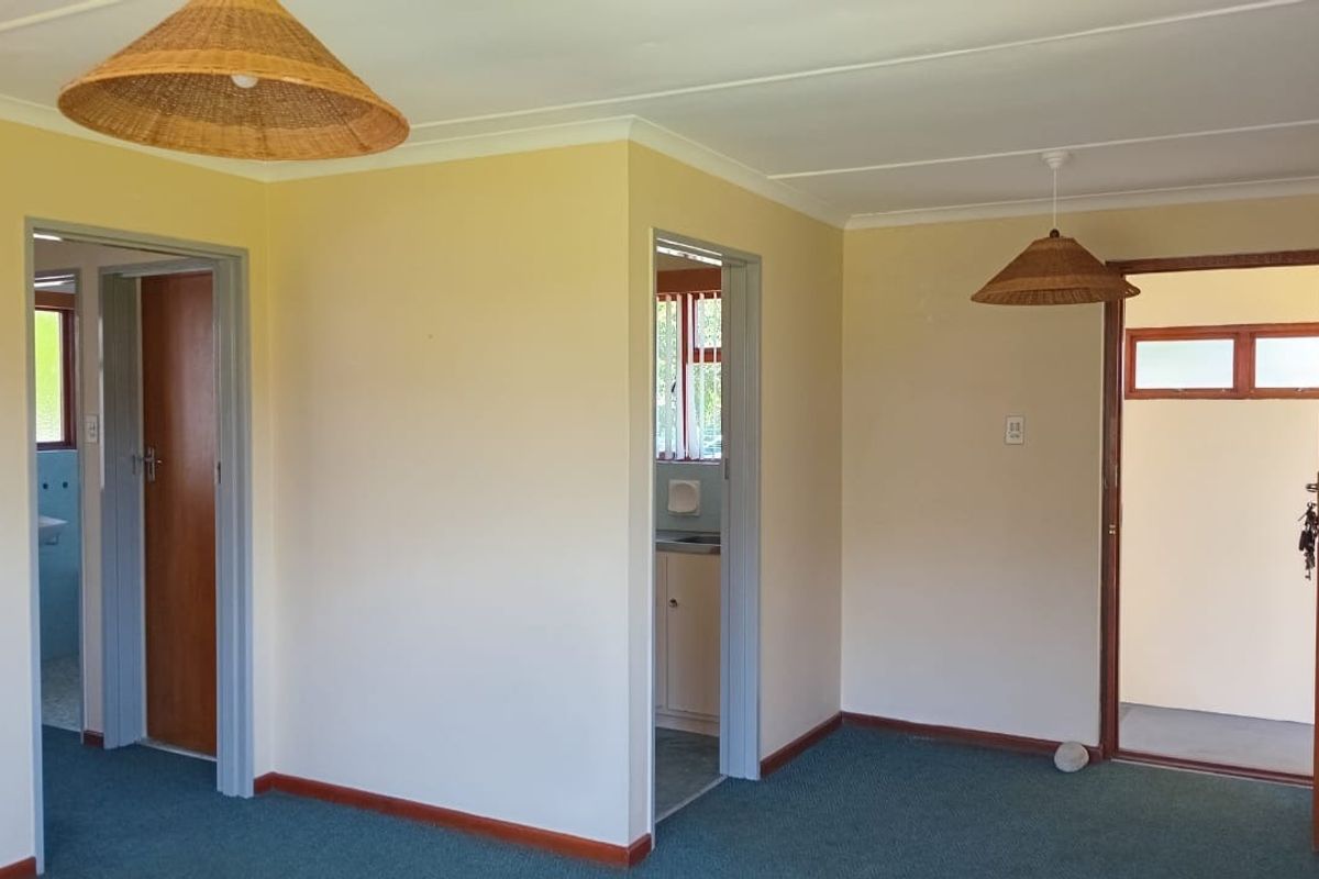 An empty living area featuring carpeted flooring, coved ceilings, and access to adjacent rooms through timber-framed doorways.