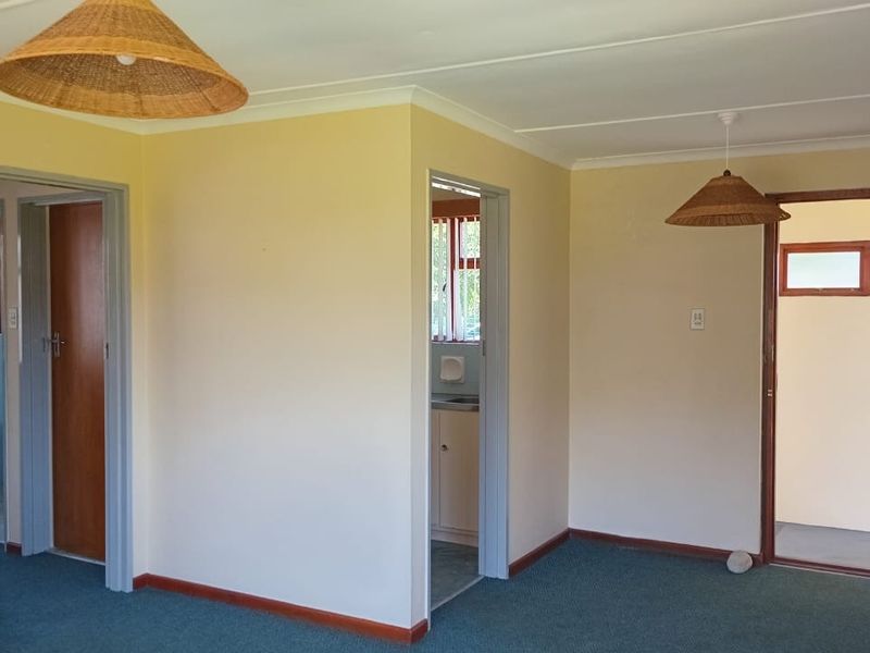 An empty living area featuring carpeted flooring, coved ceilings, and access to adjacent rooms through timber-framed doorways.