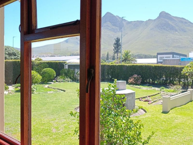 A view from an interior window looking out over a well-maintained garden with a built-in braai and mountain backdrop.