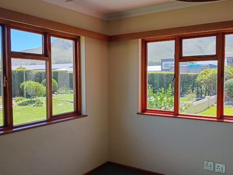 A bright, empty living room featuring timber-framed windows that offer pleasant garden and mountain views, finished with neutral walls and coving.