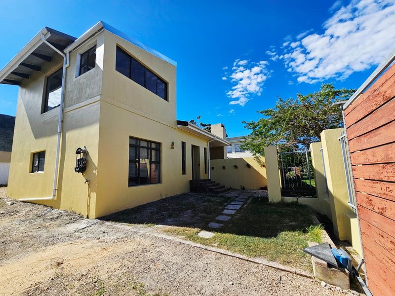 Rear view of a two-story house featuring a stepped entrance, boundary wall, and an unfinished garden area.