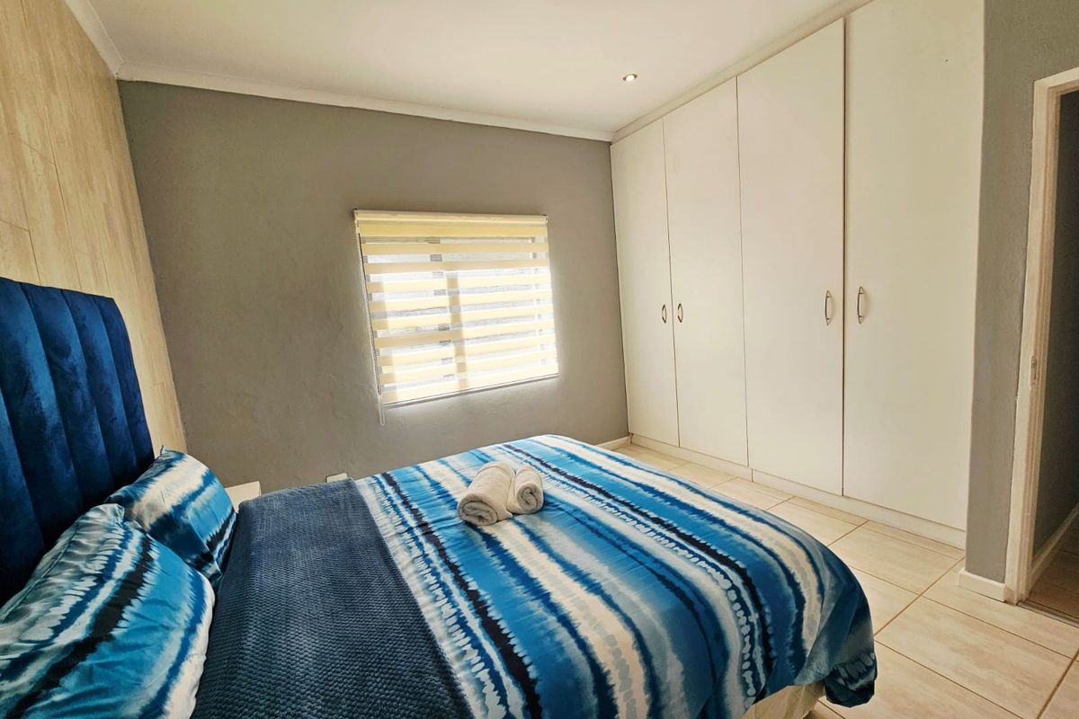 A well-maintained bedroom featuring neutral grey walls, tiled flooring, built-in cupboards, and recessed downlighting.