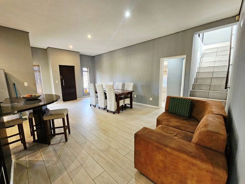 Spacious open-plan living and dining area featuring modern tiled flooring, recessed lighting, and a staircase leading to the upper level.