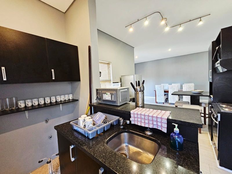 Open plan kitchen featuring dark cabinetry, granite countertops, and a stainless steel sink, flowing into a dining area with modern track lighting.