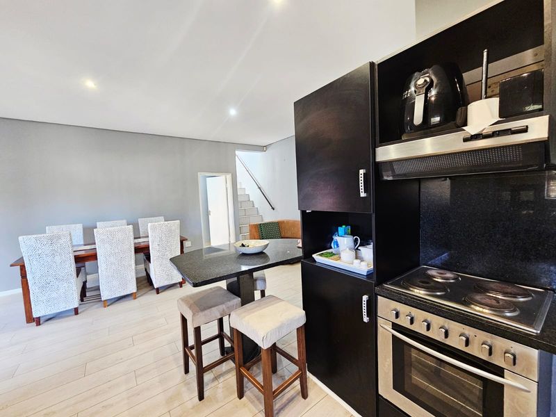 Open-plan kitchen and dining area featuring dark cabinetry, granite countertops, built-in oven and hob, and light-toned flooring.
