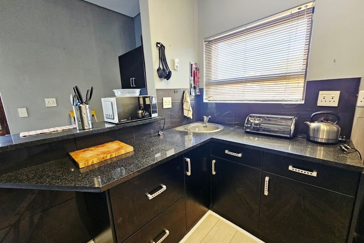 A functional kitchen featuring dark cabinetry, granite countertops, a stainless steel sink, and a tiled splashback with natural light from a window.