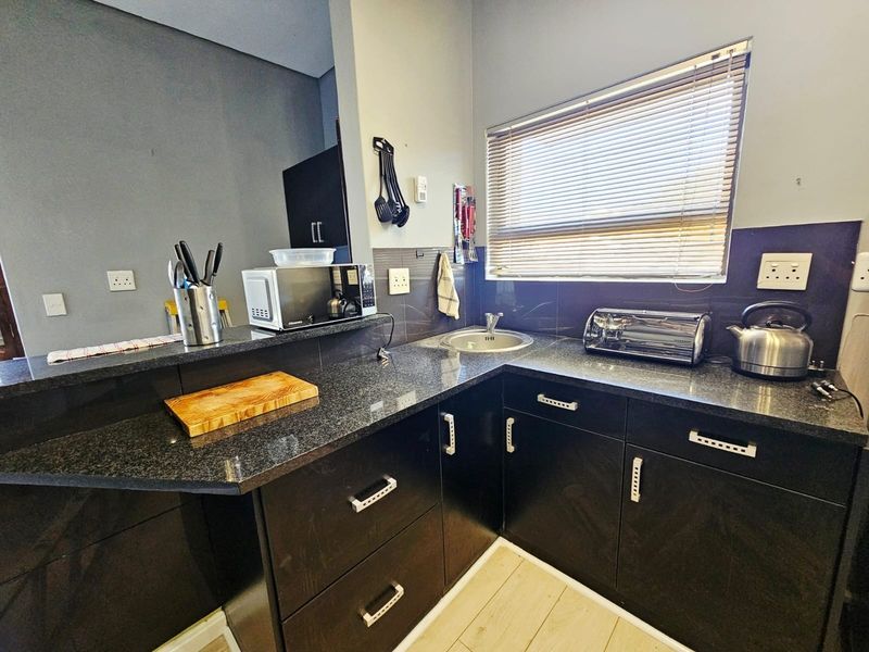 A functional kitchen featuring dark cabinetry, granite countertops, a stainless steel sink, and a tiled splashback with natural light from a window.