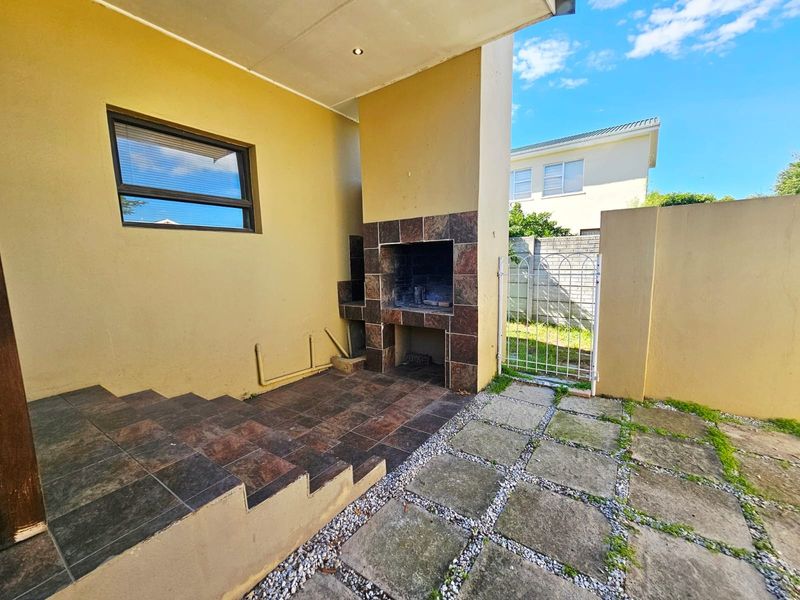 Covered patio area featuring a built-in braai, tiled steps, and direct access to the rear garden through a metal gate.