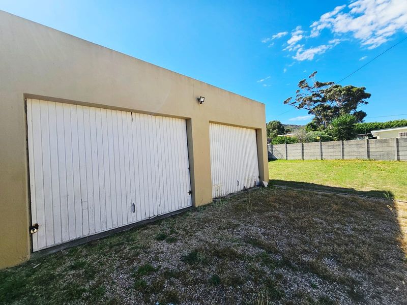 Exterior view of a double garage with white doors, featuring an adjacent lawn area and concrete boundary wall.
