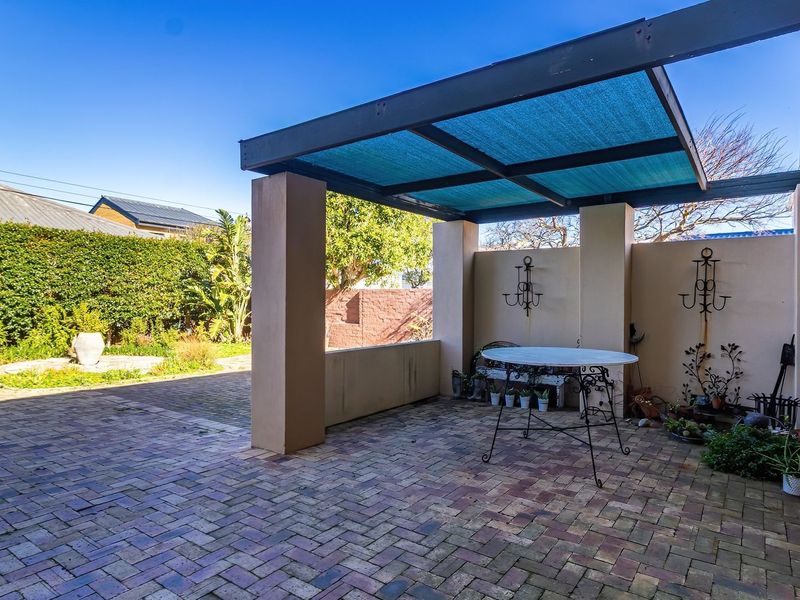 A paved outdoor patio area featuring a covered pergola structure, masonry pillars, and a private garden boundary wall.