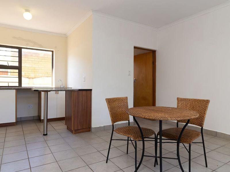 Open-plan kitchen and dining area featuring tiled floors, built-in cabinetry with granite countertops, and a window with security bars.