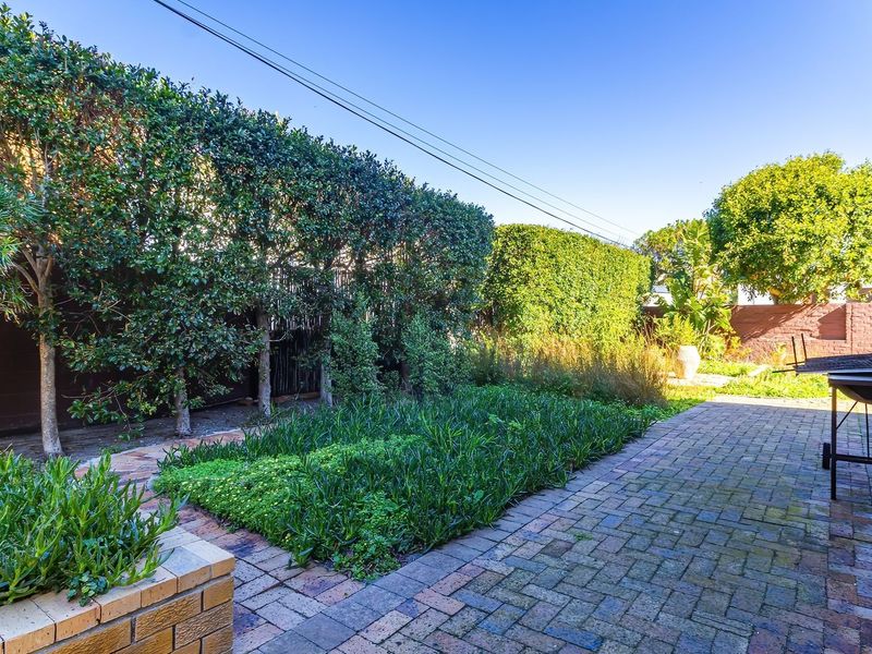 A well-maintained rear garden area featuring brick paving, a structured brick planter box, and established privacy hedging along the boundary.